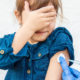 A photo of a young girl covering her eyes while receiving a shot.