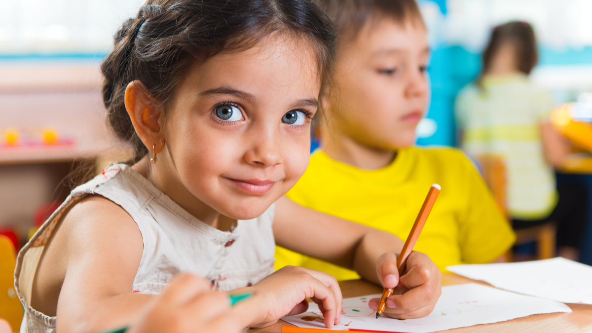 Photo of a girl and a boy at a table in a preschool room