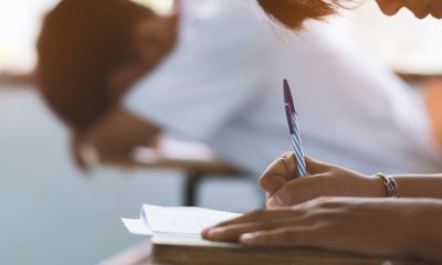 Photo of student taking exam and another stressed student laying his head on a desk