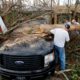 Photo of people cutting away at a tree the fell on a vehicle during Hurricane Michael