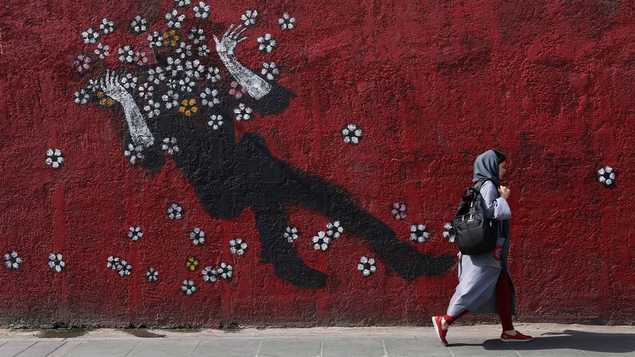 Photo of a woman walking past a mural in downtown Tehran