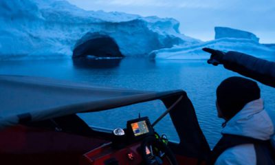 Photo of a boat navigating at night next to a large iceberg in Greenland