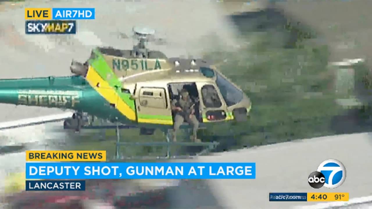 Photo of a sheriff's department helicopter with a sniper in an open door searching for a gunman at large