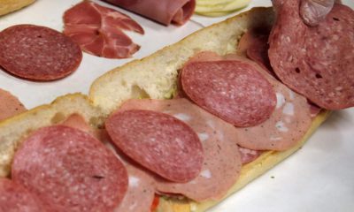 Photo of a man making a submarine sandwich with mortadella, cooked salami, ham, Genoa salami and sweet capicola