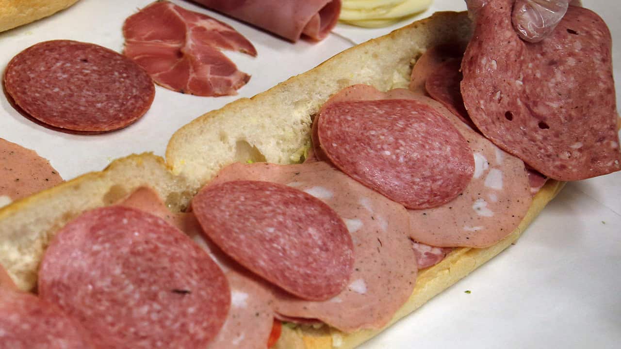 Photo of a man making a submarine sandwich with mortadella, cooked salami, ham, Genoa salami and sweet capicola