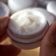 Photo of a small bottle of cream held between a thumb and a finger