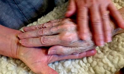 Photo of Allison Beach holding the hand of her ailing mother Kathryne Beach inside her home in Hinesburg, Vt.