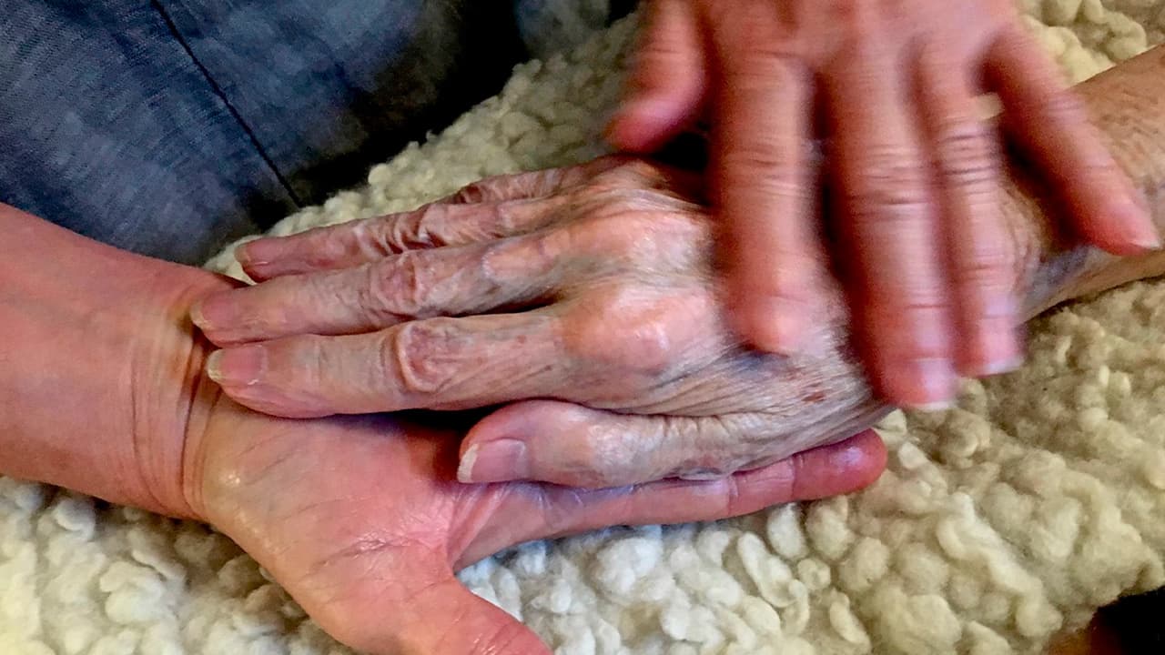 Photo of Allison Beach holding the hand of her ailing mother Kathryne Beach inside her home in Hinesburg, Vt.