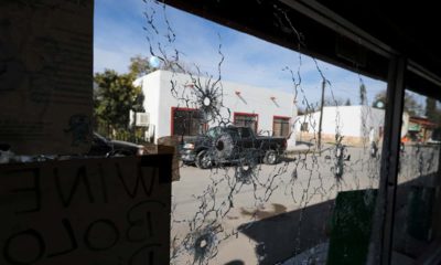 Photo of a shop window riddled with bullet holes
