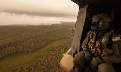 Photo of a Royal Australian Navy MRH-90 helicopter crew member looks out over fires burning near Cann River, Australia