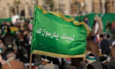 Photo of a Houthi supporter holding a banner with Arabic writing that reads, "at your order, oh messenger of Allah."