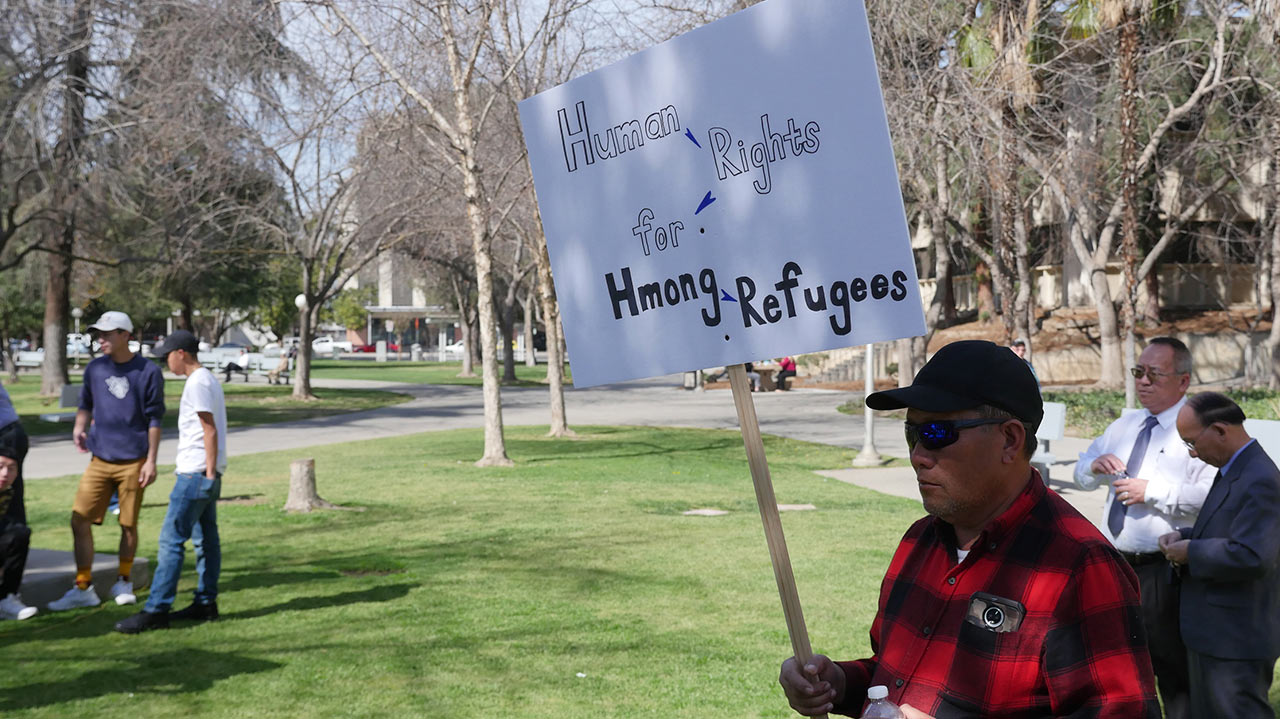 Photo of a man holding a sign at a Hmong rally