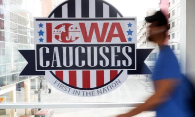 Photo of a pedestrian walking past an Iowa Caucuses sign