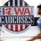 Photo of a pedestrian walking past an Iowa Caucuses sign