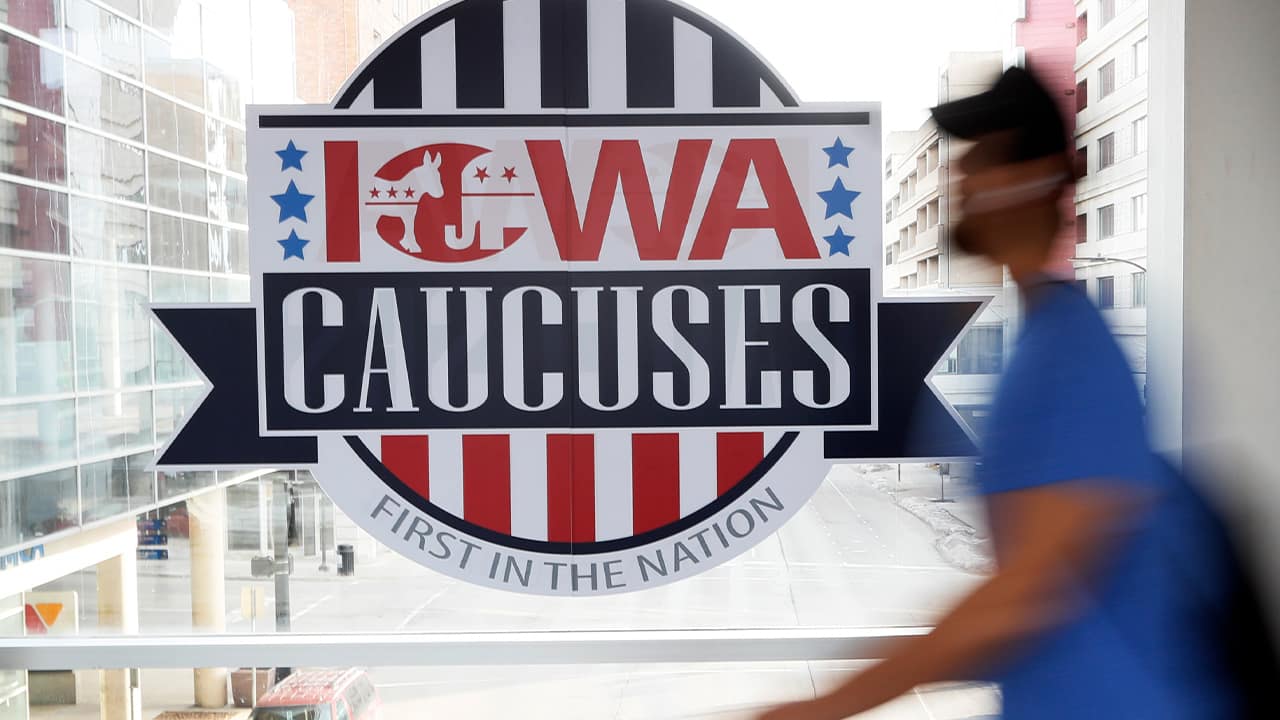 Photo of a pedestrian walking past an Iowa Caucuses sign