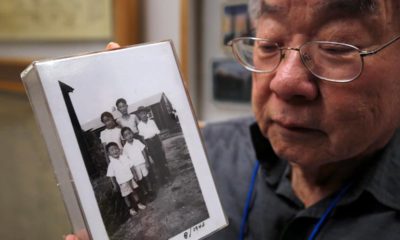 Photo of Les Ouchida holding a 1943 photo of himself, front row, center, and his siblings taken at the internment camp his family was moved to