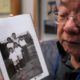 Photo of Les Ouchida holding a 1943 photo of himself, front row, center, and his siblings taken at the internment camp his family was moved to