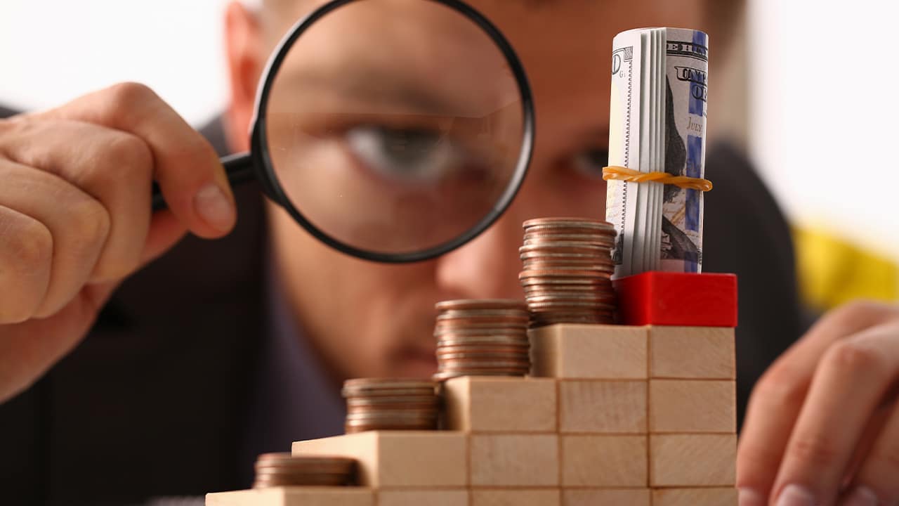 Photo of a man looking through a magnifying glass at small amounts of moneylas