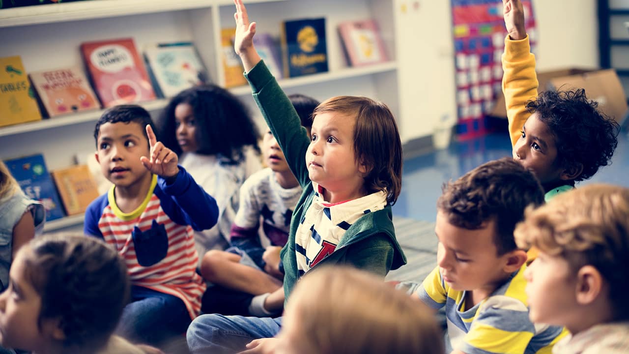 Photo of young students raising their hands in a classroom