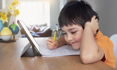 Image of a young smiling student doing online work on his tablet during COVID-19 lockdown