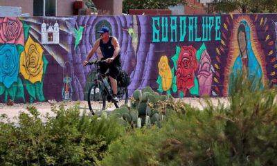 Photo of a man cycling past a mural