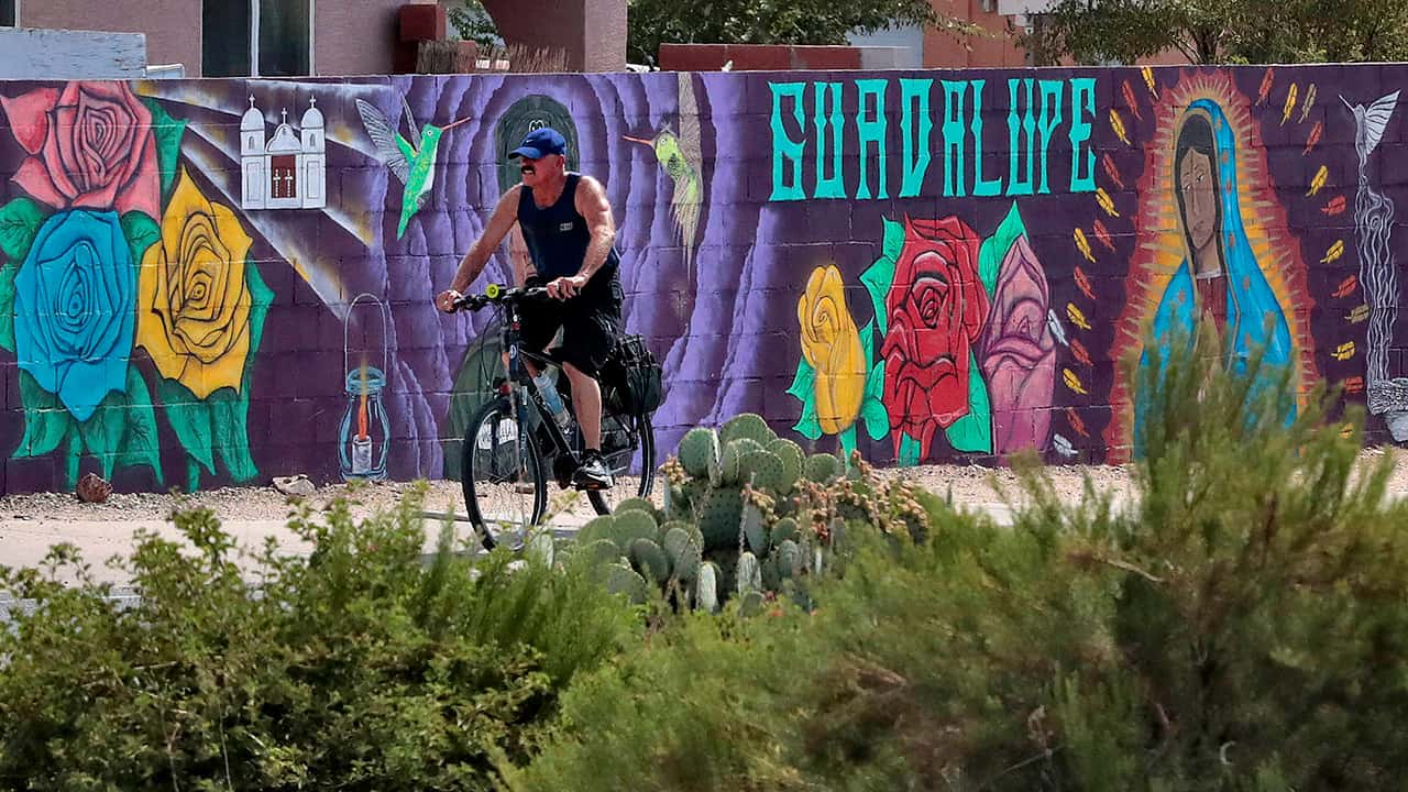 Photo of a man cycling past a mural