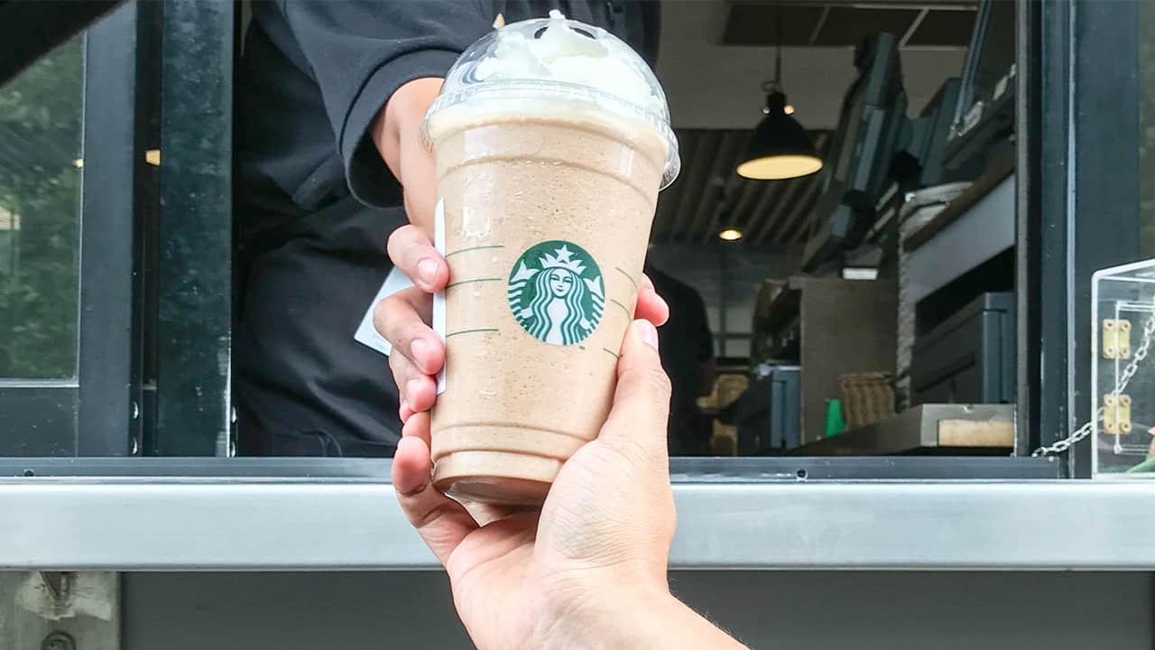 Image of a Starbucks employee handing a frappe mocha latte to a customer at drive thru counter.