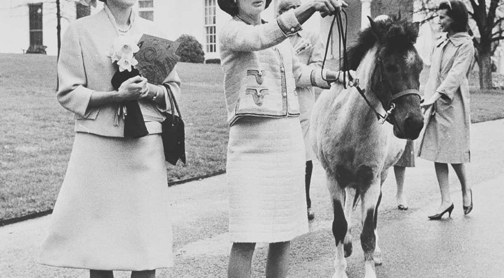 FILE – In this April 12, 1962, file photo first lady Jacqueline Kennedy gives a guided tour of the White House grounds to Empress Farah Pahlavi of Iran in Washington. Kennedy leads her daughter Caroline’s pony, Macaroni, which had been nuzzling the empress, attracted by the daffodils she was carrying. In the background is the first lady’s press secretary, Pamela Turnure. (AP Photo/Pool, File)